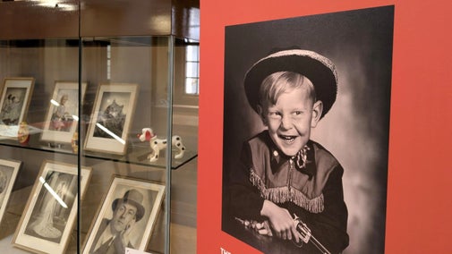 A black-and-white photo of a child dressed as a cowboy on a sign promoting a photography exhibition.